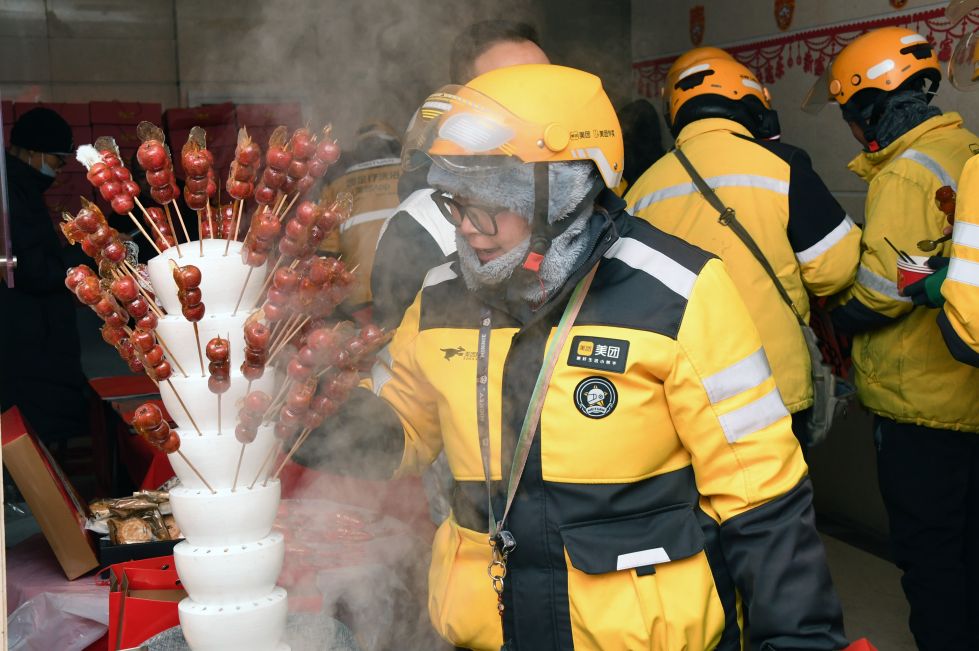2024年 1月23日,在北京市海淀区北太平庄街道户外劳动者暖心驿站,一名外卖员(前)准备品尝糖葫芦。 新华社记者 任超 摄